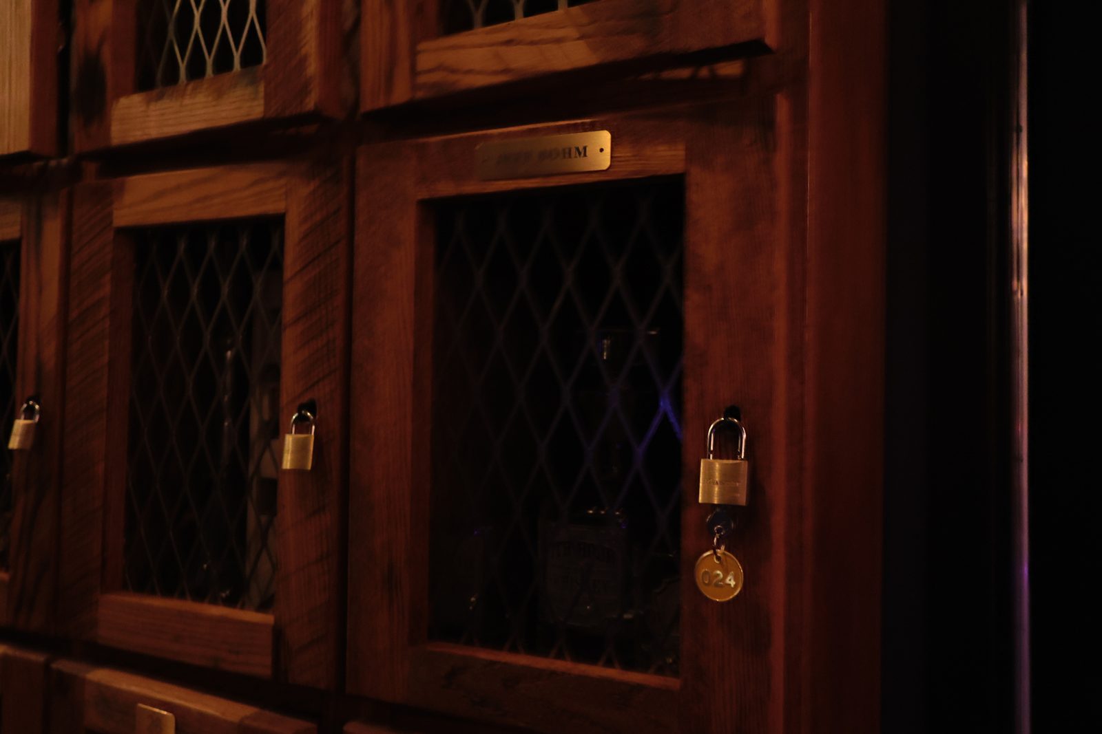 A wooden locker door with a brass padlock, key tag, and engraved nameplate